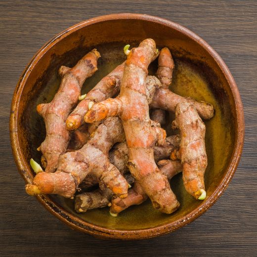 Fresh turmeric roots arranged in a brown bowl on a wooden surface.