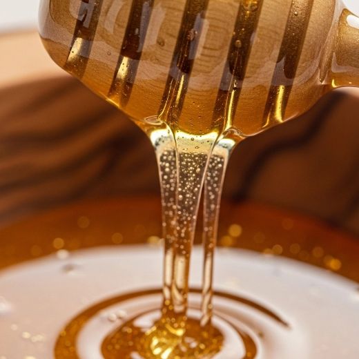 Golden honey dripping from a wooden honey dipper into a bowl, showing a rich natural sweetener used in wellness recipes.