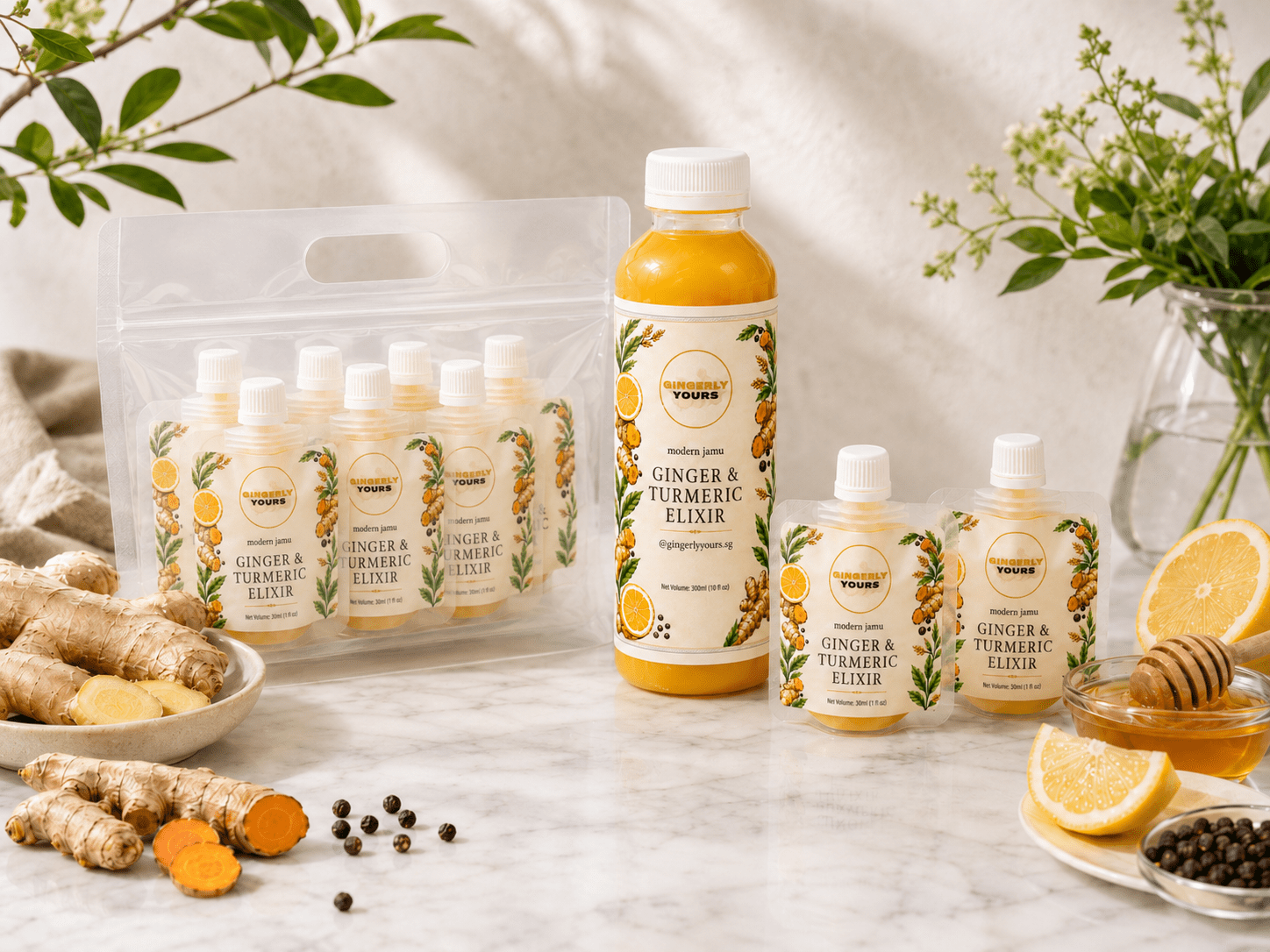 Gingerly Yours ginger and turmeric elixir bottle and pouch packs arranged with fresh ginger, turmeric, lemon, honey, black pepper, and greenery on a bright marble surface.