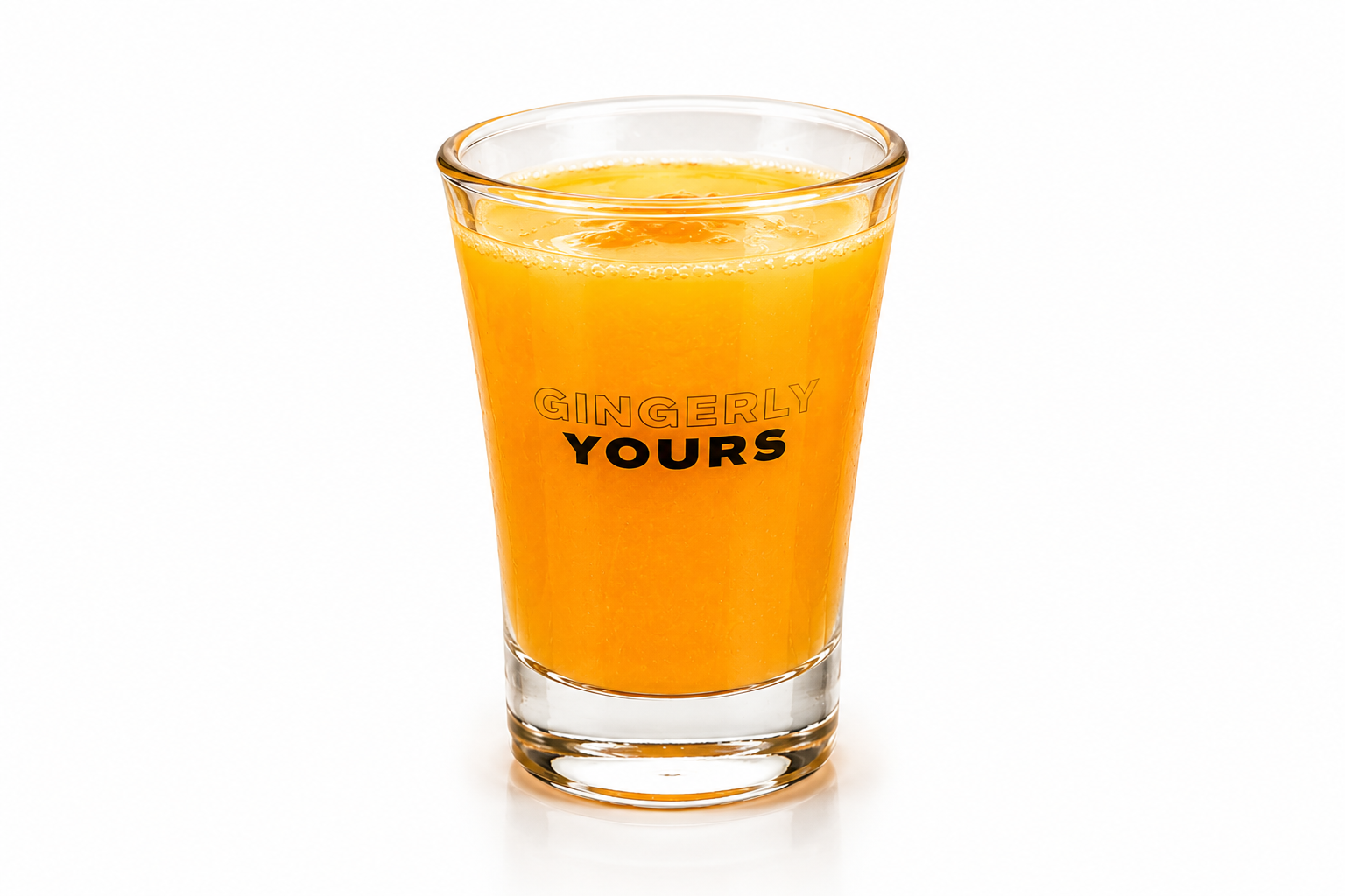 A clear glass filled with a bright orange ginger drink, printed with the words “Gingerly Yours,” against a white background.